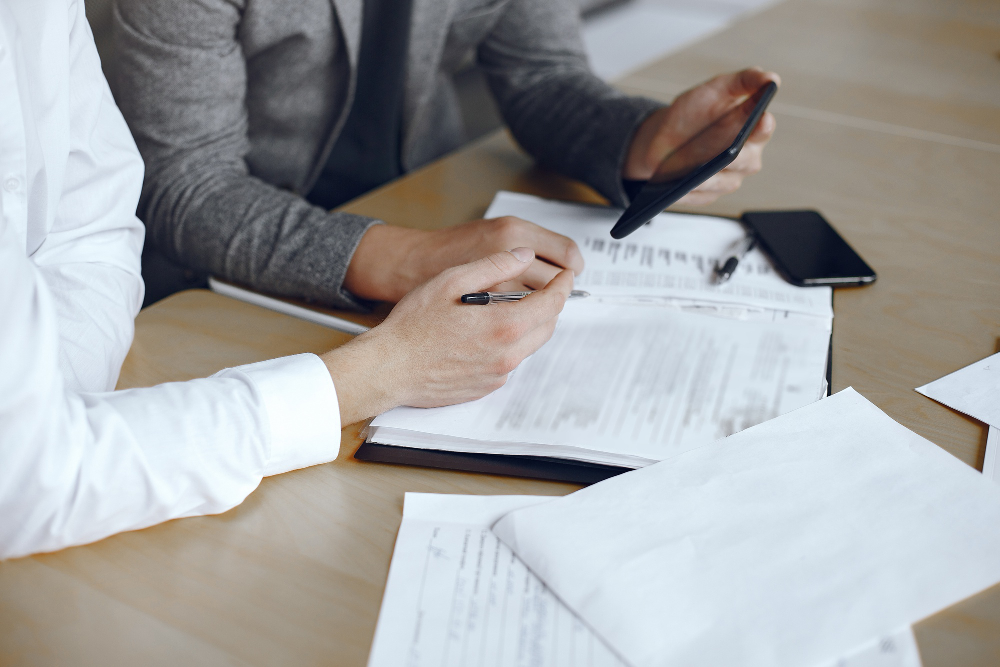 mesa con dos personas con documentación y haciendo cálculos